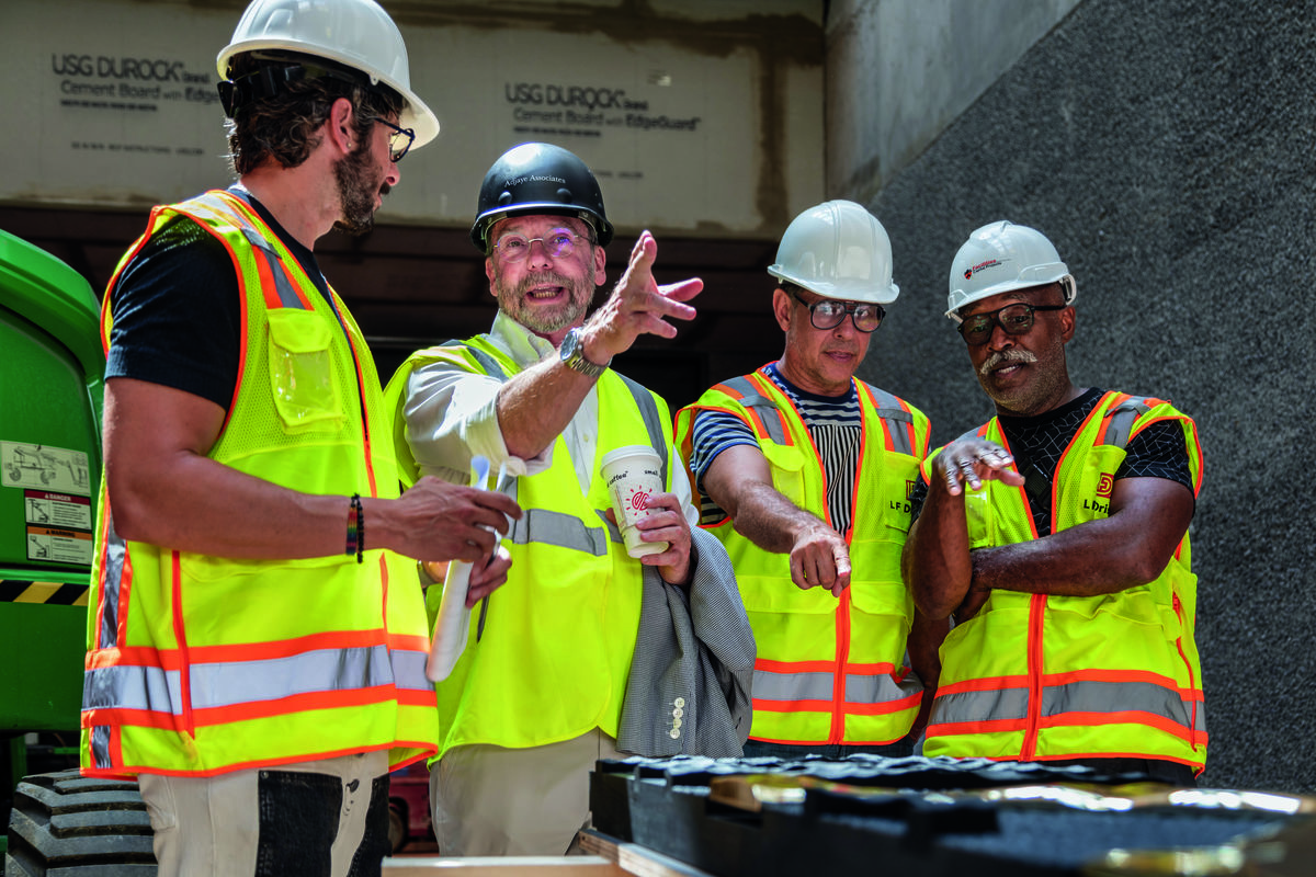 Four men wearing hard hats looking over a sample of the mosaic.