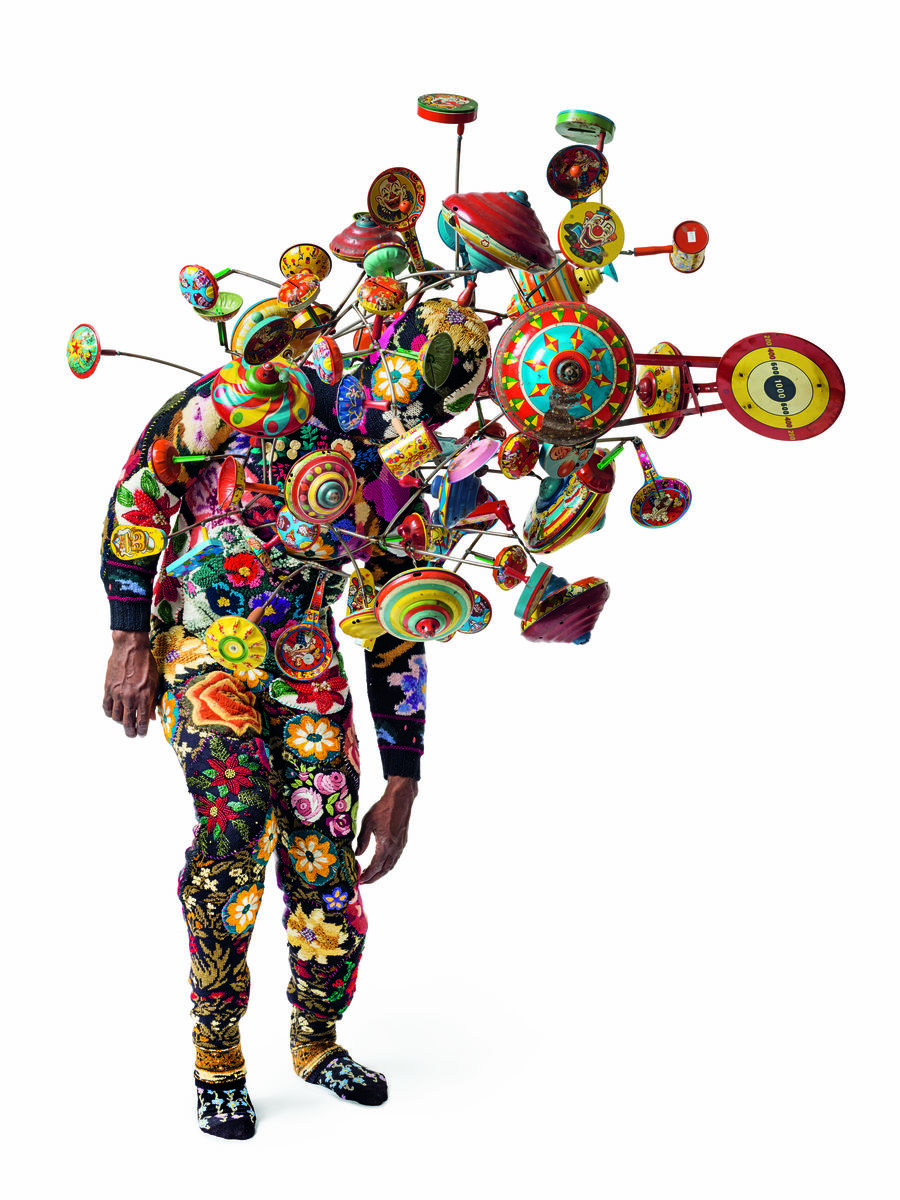 A colorful suit covered in flowers with spinning tops protruding from various points on the top half of the suit.