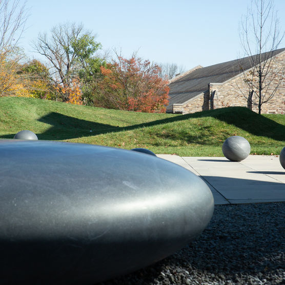 A large ovoid stone sculpture in the foreground with round smaller ball shapes in an outdoor setting.